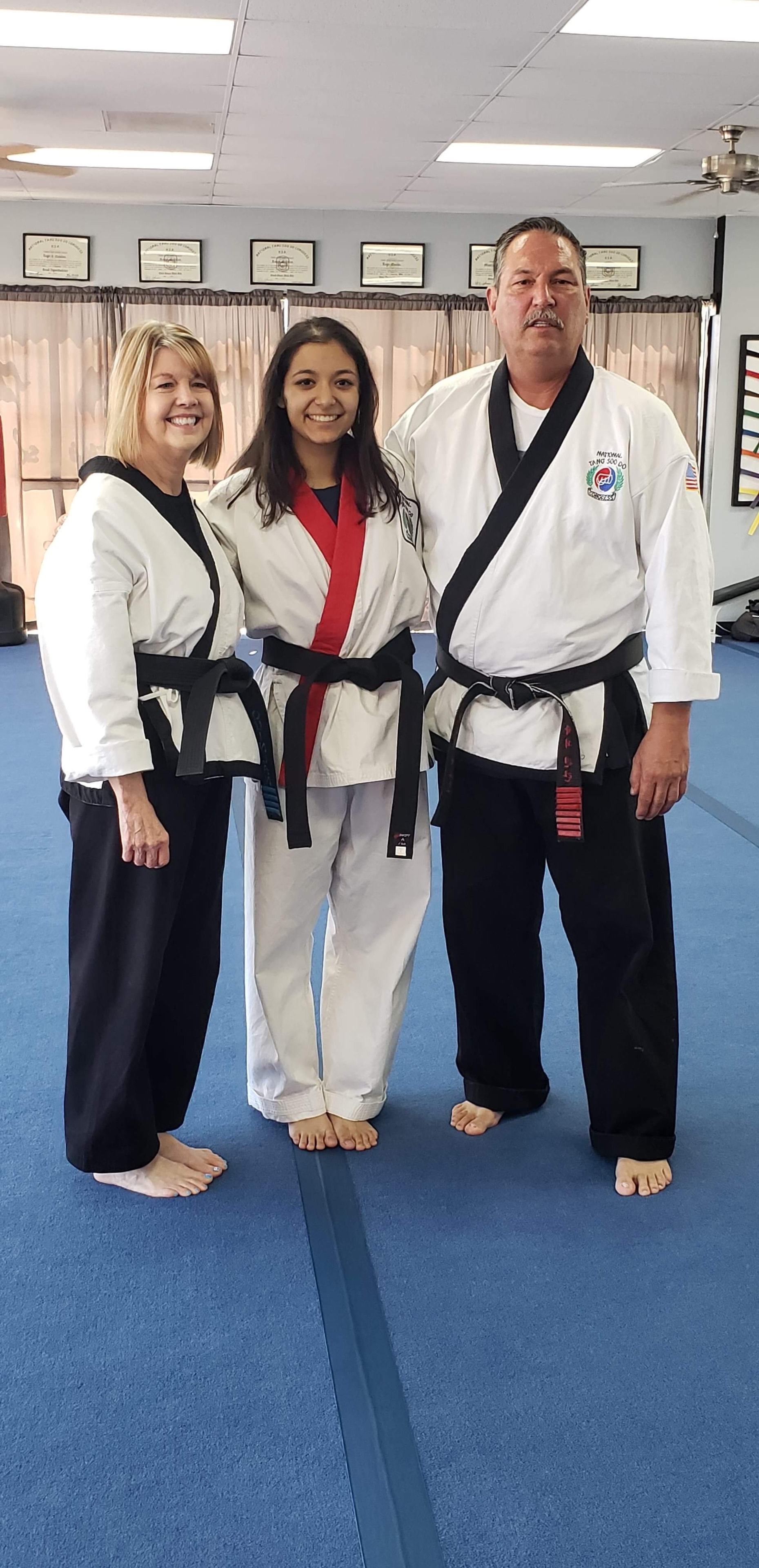 Woman instructor, girl with red trim uniform, and man instructor posing in dojo