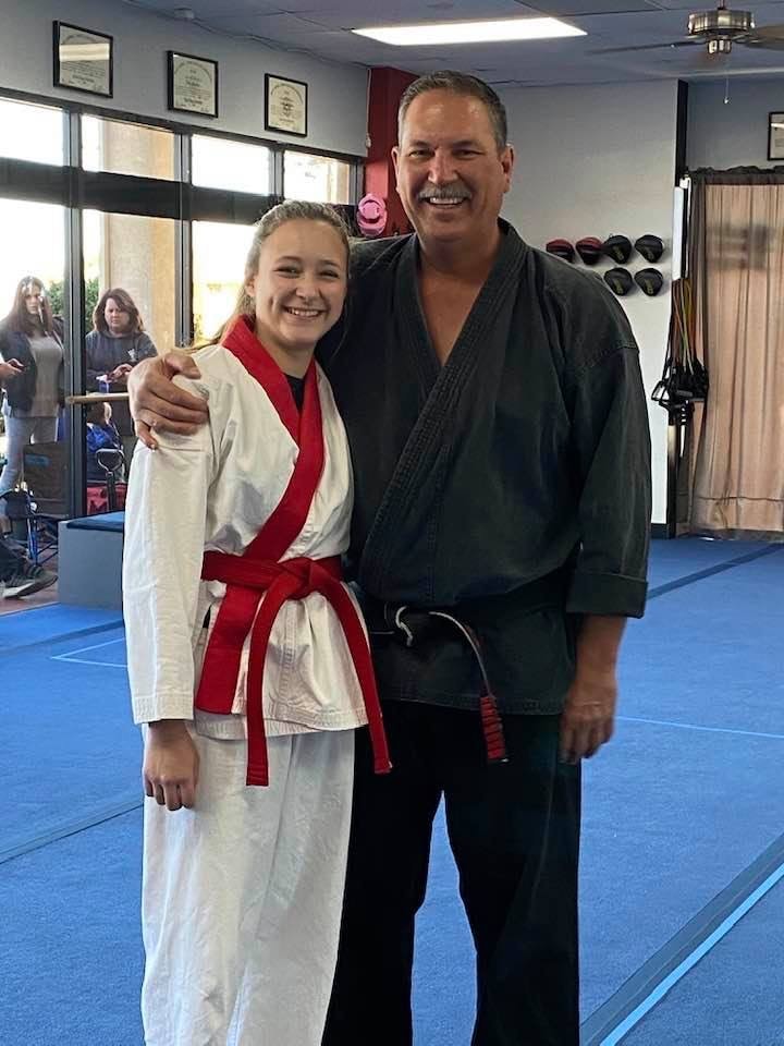 Girl with red trim uniform and instructor posing in dojo